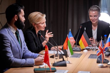 Çok ırklı başarılı iş adamlarından oluşan bir grup basın toplantısına katılırken mikrofonların önünde oturuyor.