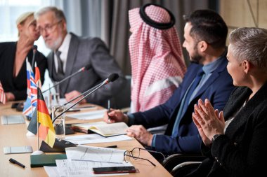 Çok ırklı başarılı iş adamlarından oluşan bir grup basın toplantısına katılırken mikrofonların önünde oturuyor.