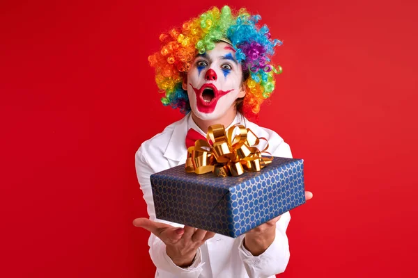 Playful positive funny clown holding gift box in hands posing — Φωτογραφία Αρχείου