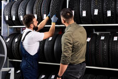Üniformalı otomobil tamircisi müşteriye seçiminde yardımcı olur