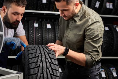 confident mechanic and client checking tires in store