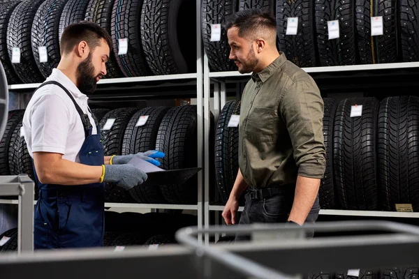 Prodejce auto mechanik pomáhá člověk vybrat pneumatiky v obchodě — Stock fotografie