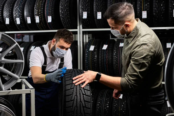 Confident mechanic and client examining tires in store — Stock Fotó