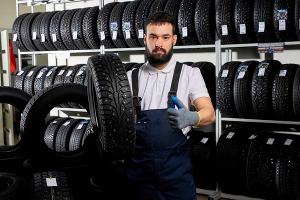 Confident caucasian car mechanic in a workshop on a stack of tires at his workplace — Zdjęcie stockowe