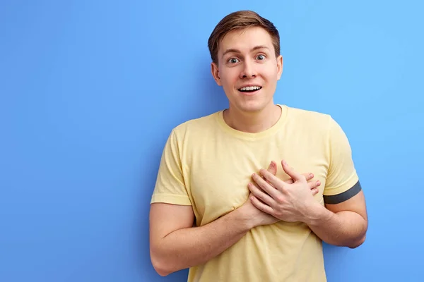 Agradable happyyoung hombre cogido de la mano en el pecho posando aislado sobre fondo de pared azul —  Fotos de Stock