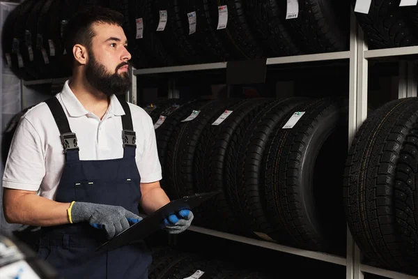 Serviço pessoal homem examinando pneus em um shopping supermercado, pensar sobre o comércio certo para o tamanho da roda — Fotografia de Stock