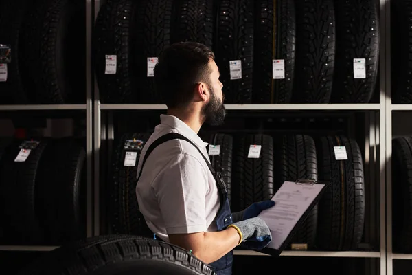 Personale di servizio uomo esaminando pneumatici in un centro commerciale supermercato, pensare al giusto commercio per le dimensioni della ruota — Foto Stock