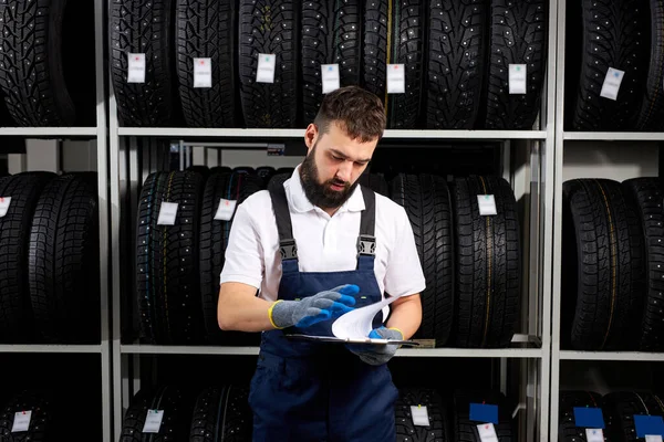 Knappe Kaukasische automonteur in uniforme standaards leeseigenschappen van banden — Stockfoto