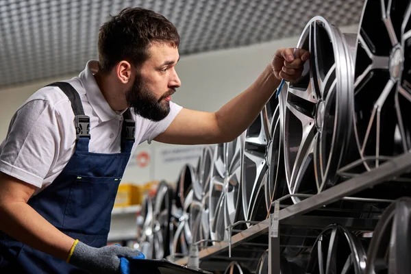 Caucásico barbudo mecánico de automóviles masculinos está comprobando los discos de coche representados para la venta en servicio — Foto de Stock