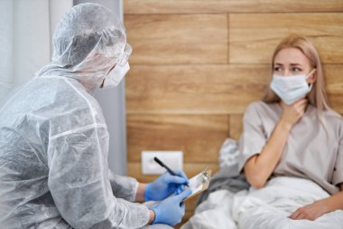 Koruyucu giysili doktor sağlık durumunu soruyor.