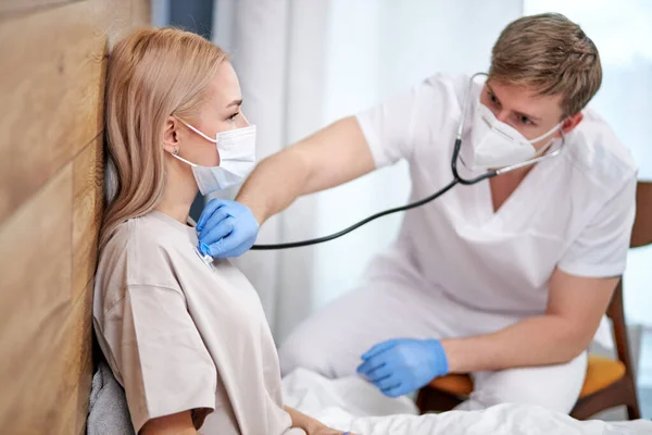 Mannelijke arts verpleegkundige in beschermende gezichtsmasker luisteren naar adem met een stethoscoop vermoeden COVID-19 — Stockfoto