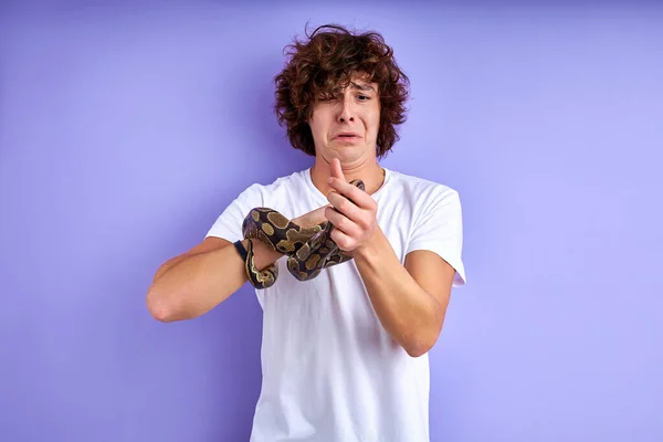 Молодий білий чоловік робить смішне обличчя похмурим, тримаючи змію в руках — стокове фото