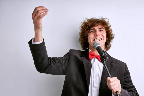 Емоційний молодий чоловік співак у костюмі позує ізольовано на білому тлі стіни, студійний портрет — стокове фото