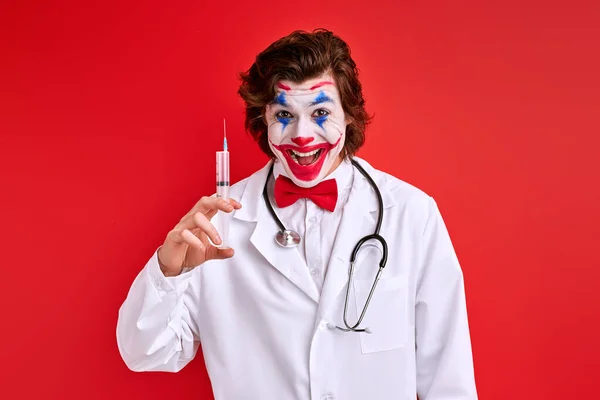 Pediatra payaso masculino preparó una jeringa aislada sobre fondo rojo — Foto de Stock