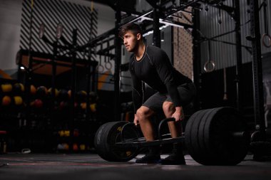 Halterle egzersiz yapan bir adam. Erkek vücut geliştirici koyu renk spor salonunda ağırlık kaldırma egzersizi yapıyor.