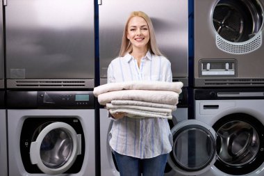 Genç Avrupalı beyaz kadın, sarı saçlı, gülümseyen, çamaşırhanede iş yaparken mutlu.