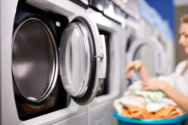 Женщина в стиральной машине сортирует чистую одежду, выполняет домашние обязанности — стоковое фото