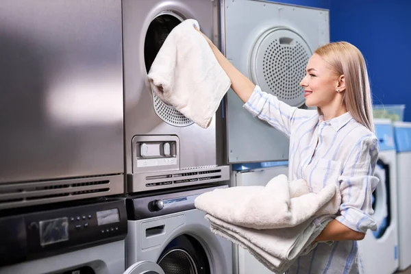 Женщина стоит одна с чистыми полотенцами в самообслуживании прачечная с сушильными машинами — стоковое фото
