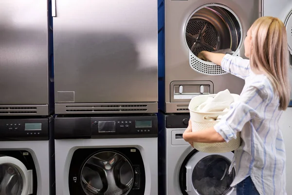 Домашняя работа: молодая кавказская женщина стирает бельё - кладет белую одежду в стиральную машину — стоковое фото