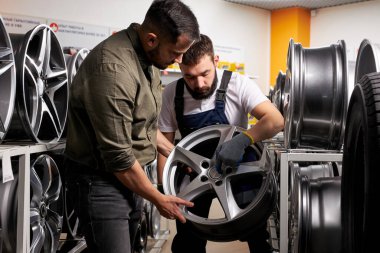 Kendine güvenen oto tamircisi araba tekerleğinin özellikleri ve avantajlarından müşteriye bahsediyor