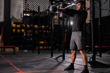 Güçlü, formda, kaslı, büyük kaslı, elinde ağır bir su ısıtıcısı tutan adam.