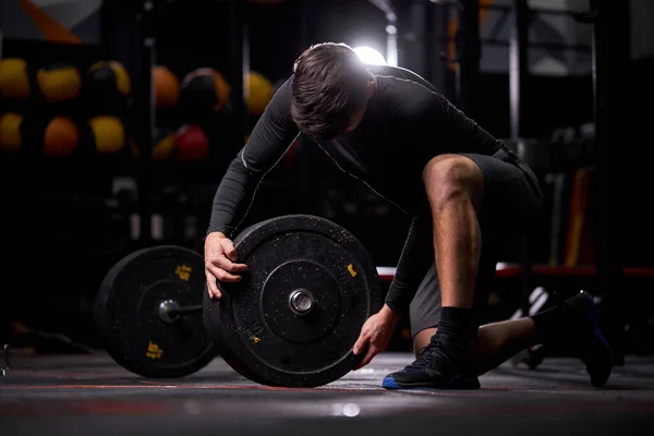 Athlete male adding weight plates on his barbell, preparing for weightlifting workout at gym