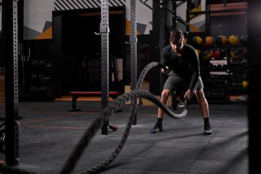 Sportif şortlu güçlü bir adam Crossfit jimnastik salonunda halat egzersizi yapıyor.