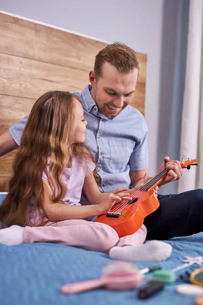 Dad plays guitar with his daughter. little child learns to play musical instrument with tutor