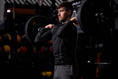 Beyazlı genç sporcu spor salonunda halter kaldırıyor.