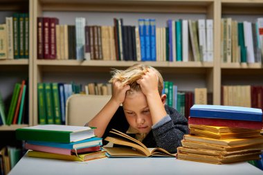 Uykulu çocuk kütüphanede kitaplarla masada oturuyor.