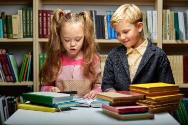 Kafkasyalı çocuklar kütüphanede masada otururken birlikte kitap okuyorlar.