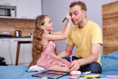 Genç bir adam ve kızı evde kozmetikle oynuyorlar. Makyaj yapıyorlar.