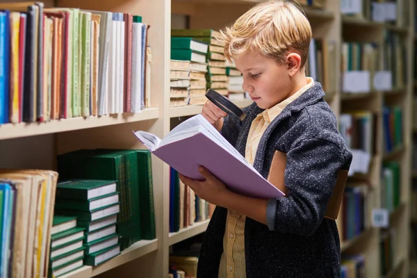 portrait of adorable little preschool boy reading book in library with patience