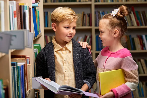 Okul kütüphanesinde kitap okuyan iki tatlı çocuk ve kız.