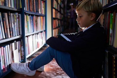 Çalışkan çocuk gece gündüz öğreniyor, kütüphanede yerde kitap okuyor.