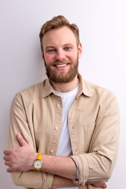 Kızıl saçlı, sıradan giyinen, kolları bağlı, kameraya gülümseyen erkek.