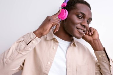 Sıradan giyinen pozitif siyah erkek. Beyaz kulaklıkla izole edilmiş müzik dinle.