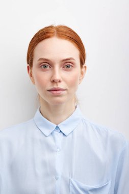 Stüdyo duvarında poz veren mavi bluzlu, doğal kızıl saçlı güzel bir kız öğrenci.