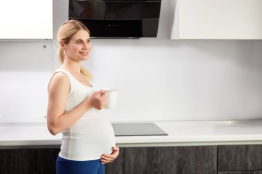 Yan manzara portresi. Hamile kadın. Sabah elinde bir bardak taze suyla ayakta duruyor.