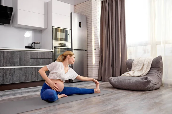 attractive sportive mom-to-be stretching legs during workout at home