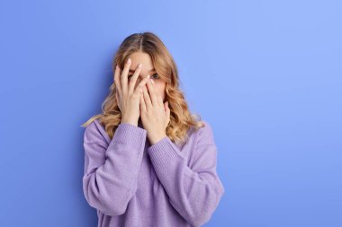 Korkmuş kadın şok içinde yüzünü kapatıyor, korku içinde ayakta duruyor.