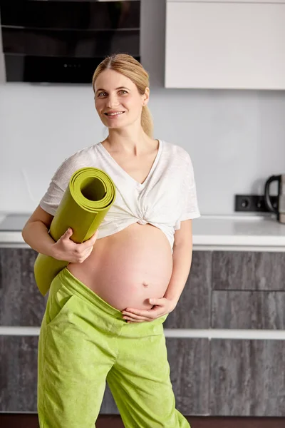 Retrato de linda embarazada acariciando el vientre conmovedor, mamá-a-ser esperando bebé, soporte con la estera de la aptitud después del yoga — Foto de Stock