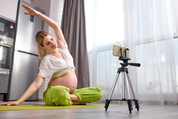 Mujer embarazada practicando yoga en casa con smartphone. Madre embarazada haciendo la clase de video entrenamiento prenatal — Foto de Stock