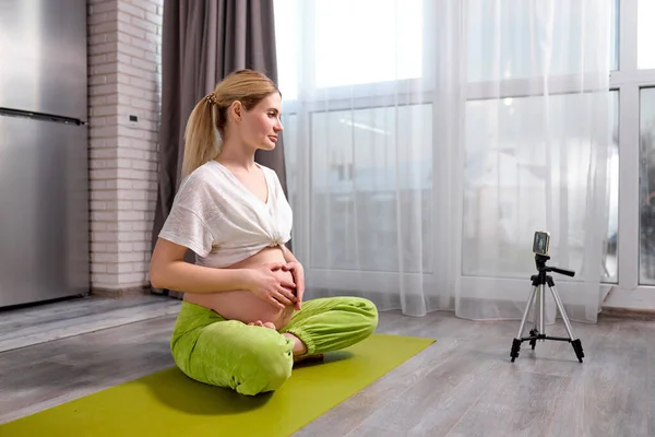 Gravid femeie care practică yoga acasă cu smartphone-ul. Mama așteptată face cursuri de formare video prenatală — Fotografie, imagine de stoc