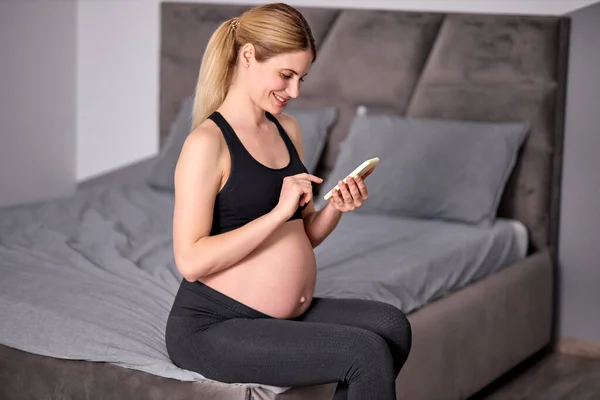 Вид збоку на красиву вагітну жінку, що сидить з мобільним телефоном, відпочиває — стокове фото