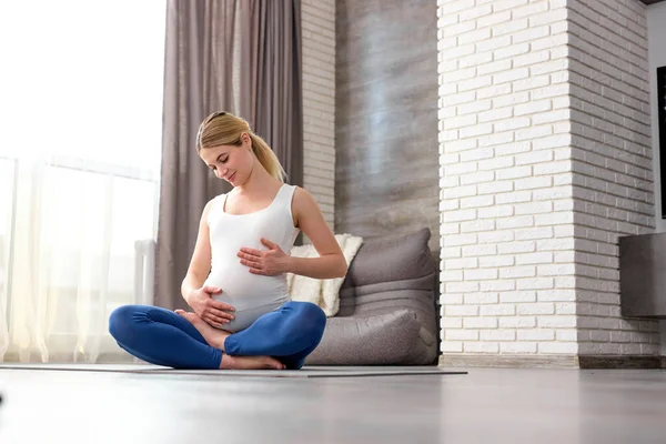 Retrato de mujer rubia sentada en el suelo acariciando gran barriga con el bebé dentro de ella —  Fotos de Stock