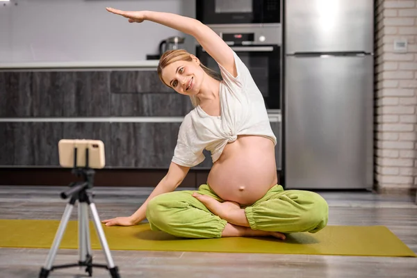 Гнучка блондинка кавказька вагітна жінка робити вправи йога дивитися відео онлайн — стокове фото