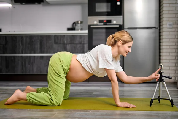 Hembra embarazada haciendo ejercicio de Marjariasana de la postura del gato en casa, viendo el vídeo Cursos en línea — Foto de Stock