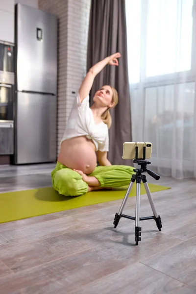 Femeie gravidă care se întinde și se antrenează la domiciliu înregistrând pe smartphone — Fotografie, imagine de stoc