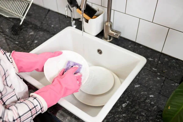 Close-up van vrouwelijke handen in roze beschermende rubberen handschoenen wassen witte plaat met paarse reinigingsspons — Stockfoto